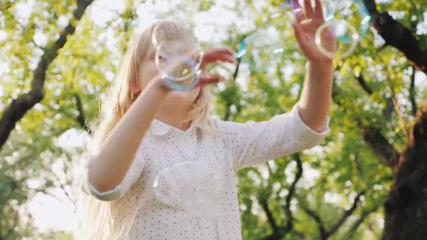 Uma menina loira alegre está brincando com bolhas de sabão. Carefree conceito de infância feliz — Vídeo de Stock