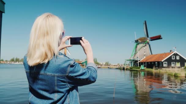 Een jonge vrouw is het fotograferen van oude windmolens in Nederland. Reizen Europa en het concept van Nederland — Stockvideo
