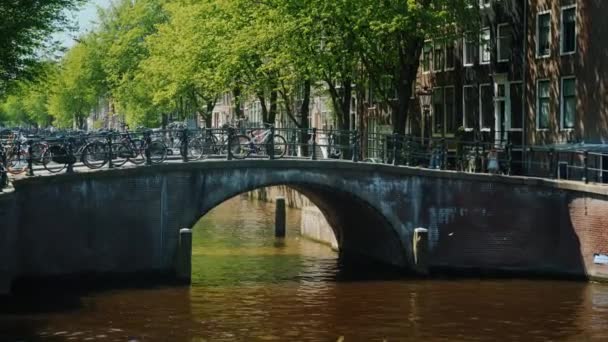 Den vackra utsikten över Amsterdam är bron över kanalen, där många cyklar parkerade. En typisk bild i staden, tiden före solnedgången — Stockvideo