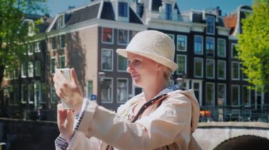 Bir kadın turist kanalı yakınındaki pitoresk bir yerde kendini fotoğraflarını çekiyor. Amsterdam ve Hollanda'da turizm