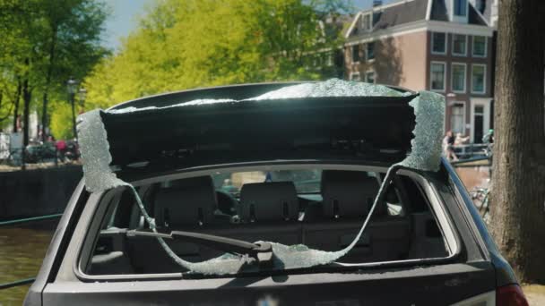 Kırık bir arka pencere olan bir araba. Hırsızlar ve Vandallar şehrin ortasındaki kurbanı. Merkezi Amsterdam kanal kıyısında — Stok video