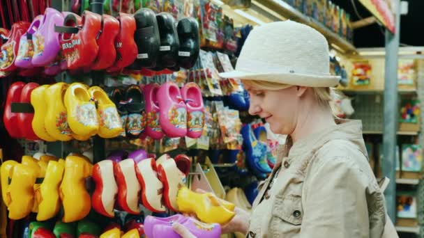 Amesterdam, Netherlands, May 2018: A woman chooses a traditional souvenir from the Netherlands - wooden shoes - claps — Stock Video