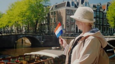 Bir kadın onun elinde Hollanda bayrağı ile Amsterdam kanalda güzel manzarasına hayran