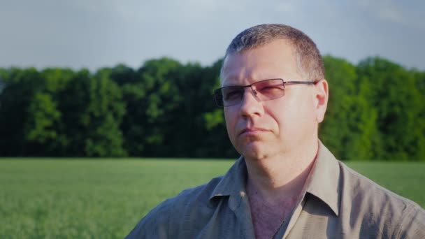 Портрет фермера средних лет в очках на фоне зеленого поля — стоковое видео
