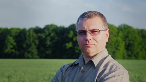 Portret van een succesvolle boer, kijken naar de camera. Tegen de achtergrond van een groene tarweveld — Stockvideo