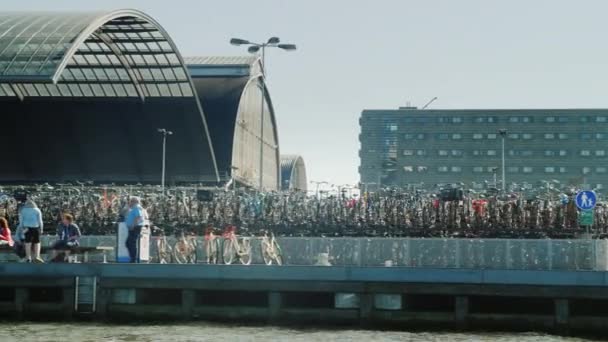 Amesterdam, Holandia, maja 2018 r.: Nowoczesna architektura Amsterdam - pływaj obok duży parking dla rowerów — Wideo stockowe