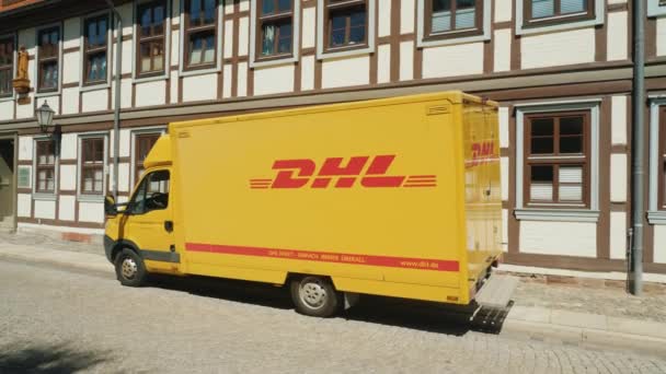 Вернигероде, Германия, май 2018 года: Фургон почтовой связи DHL стоит на тихой улице в немецком городе на фоне типичной для Германии архитектуры. Вид сбоку — стоковое видео