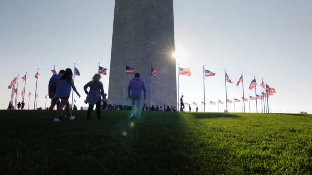 Washington DC, Estados Unidos, octubre de 2017: La gente está descansando cerca del Monumento a Washington en el centro de la capital estadounidense. El sol brilla por el obelisco — Vídeo de stock