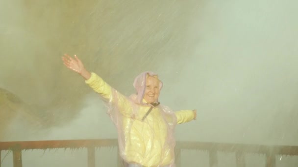 Een vrouw in een regenjas vormt onder de sterke spray van water van Niagara Falls. Extreme concept van foto-, energie- en avontuur. Slow motion video — Stockvideo