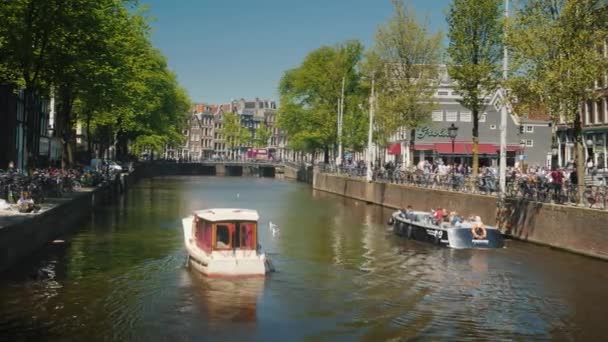 Amesterdam, Nederland, mei 2018: Pittoreske gracht in Amsterdam. Boten langs de kust en de geparkeerde fietsen. — Stockvideo