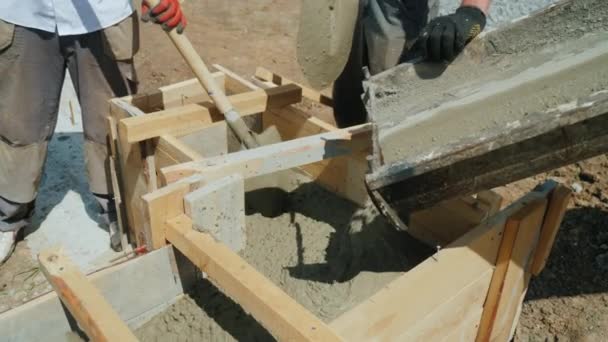 Работа с бетоном на строительной площадке. Рабочие берут бетон в деревянную форму. Тяжелый ручной труд на строительной площадке — стоковое видео