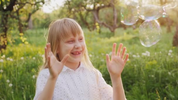 Беззаботная девушка весело ловит мыльные пузыри. Прогулка по весеннему саду — стоковое видео