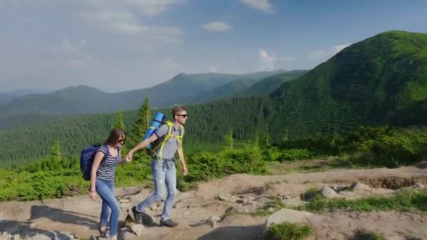 Чоловік допомагає своїй жінці під час сходження на гору. Концепція допомоги та підтримки — стокове відео