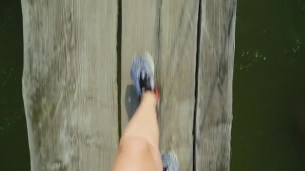 POV βίντεο: τα πόδια μιας γυναίκας είναι το περπάτημα κατά μήκος ένα στενό ξύλινο γεφυράκι πάνω από ένα ποτάμι βουνό. Κινδύνου και της περιπέτειας — Αρχείο Βίντεο