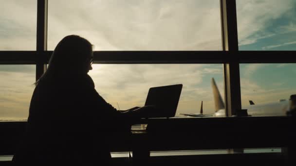 Силуэт деловой женщины в костюме, работающей с ноутбуком в терминале аэропорта — стоковое видео