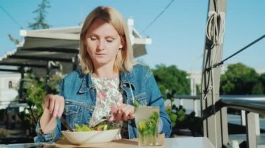 Genç bir kadın bir restoranda yaz terasında bir salata yiyor. Açık havada yemek