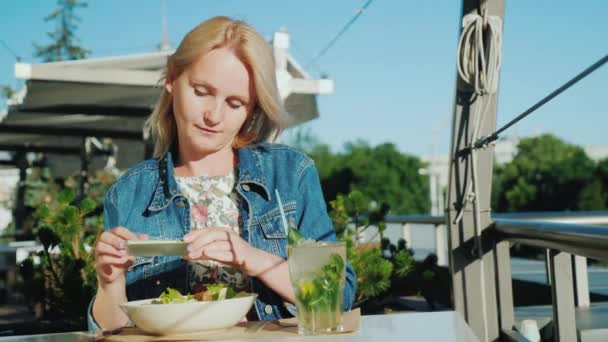 Mujer joven toma fotos de hermosos platos en un café. Buen descanso en la veranda de verano y vacaciones de verano — Vídeos de Stock