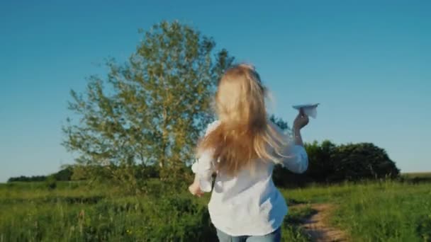 Una chica con el pelo largo corre con un avión de papel en la mano. Concepto de sueños bebé — Vídeo de stock
