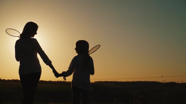 Mom and daughter are standing at sunset, holding tennis rackets. Sports family, leisure concept — Stock Video