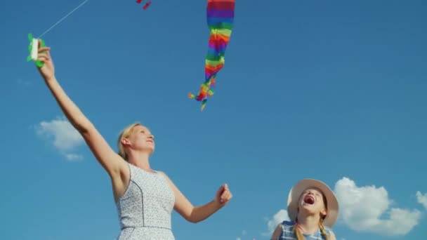 Uma mulher despreocupada brinca com sua filha, uma menina tenta pegar um papagaio de ar. Contra o fundo do céu azul puro — Vídeo de Stock