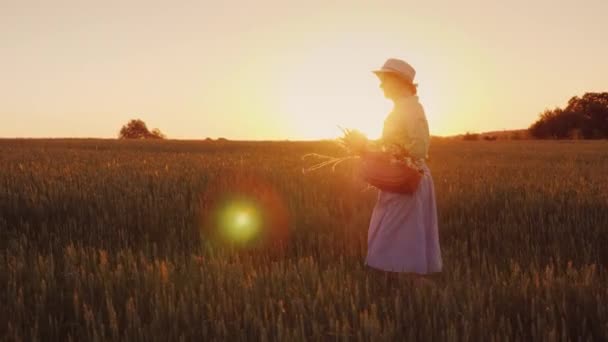 Romantyczna kobieta z bukietem kwiatów, chodzenie na polu o zachodzie słońca. Widok z boku — Wideo stockowe