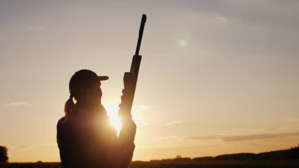 Silueta de una mujer con un rifle en los rayos de un atardecer. Tiro deportivo — Vídeo de stock