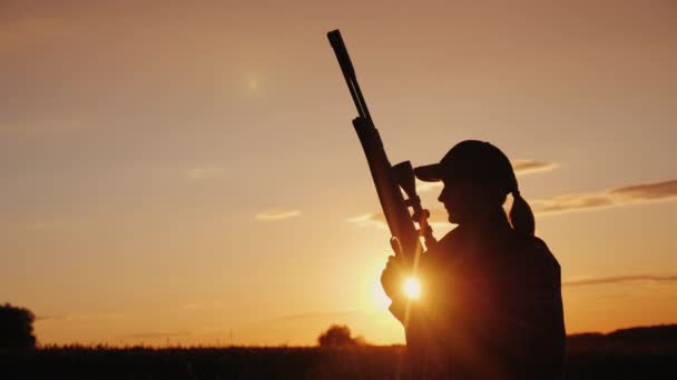 Belle silhouette d'une femme avec un fusil dans les rayons du soleil couchant. Concept de chasse et tir sportif — Video