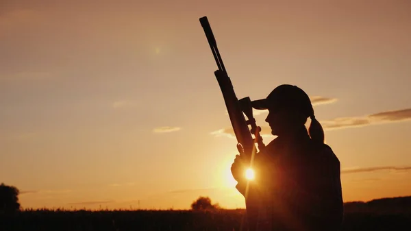 Hermosa silueta de una mujer con un rifle en los rayos del sol poniente. Concepto de caza y tiro deportivo — Foto de Stock