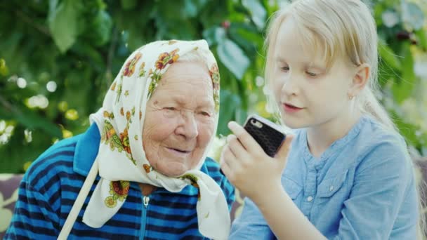 Το κορίτσι δείχνει γιαγιά φωτογραφίες σε smartphone της. Κοινωνία των γενεών αντίληψη — Αρχείο Βίντεο
