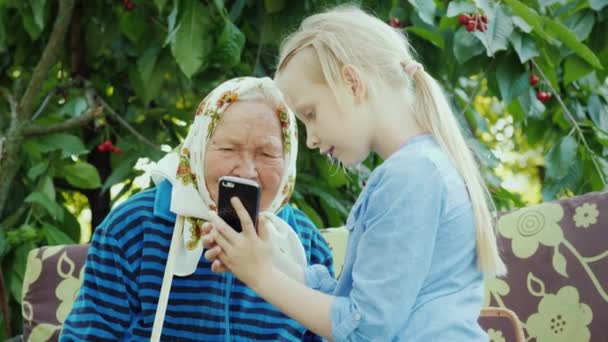 La ragazza comunica con la vecchia nonna, mostra le sue foto al telefono. Comunione delle generazioni Concetto — Video Stock