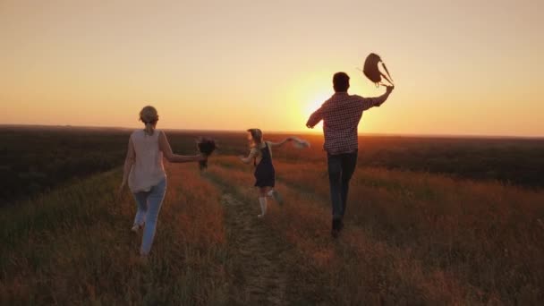 Eine fröhliche Familie rennt freudig der Sonne entgegen. Emotional winkende Rucksäcke und ein Blumenstrauß. Urlaubs- und Urlaubskonzept — Stockvideo