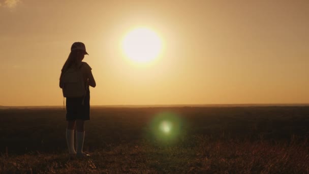 Egy lány egy hátizsák van egy festői helyen, várjuk a naplementét. Egy kis utazó és egy gyermek álma fogalom. Hátulsó nézet — Stock videók