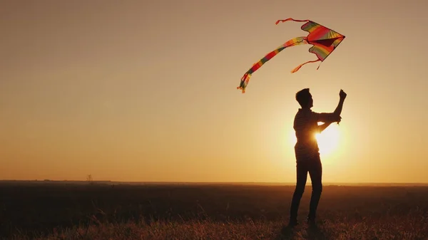 Een tiener lanceert een vlieger bij zonsondergang. — Stockfoto