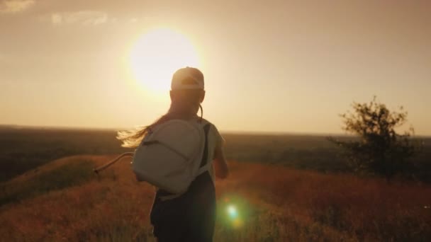 Девушка с рюкзаком бежит с холма к солнцу. 4K видео — стоковое видео