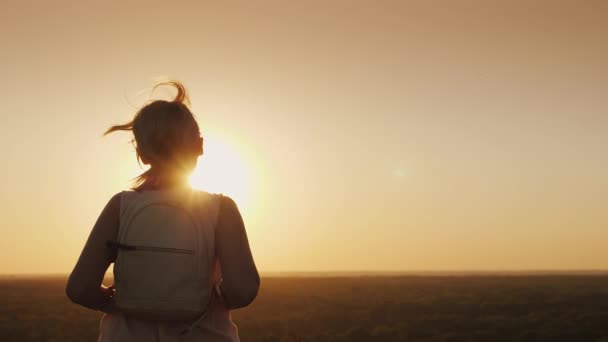 Una joven con una mochila corre hacia el sol. El cabello brilla en los rayos del atardecer — Vídeos de Stock