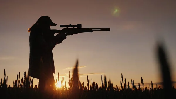 El cazador apunta desde un rifle con una mira óptica. Se encuentra en un lugar pintoresco al atardecer — Foto de Stock