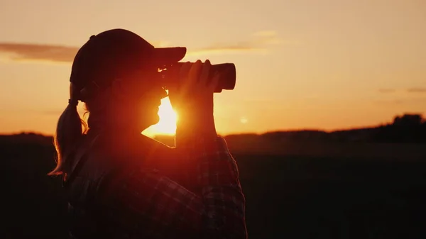 Una mujer mirando a través de prismáticos al atardecer. Concepto de viaje y safari — Foto de Stock