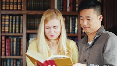 Arkadaşlar öğrencilerin birlikte kütüphanede kitap bakın. Rafları kitaplarla arka planı.