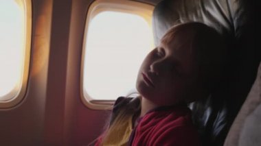 Küçük kız uçak kabin içinde uyuyor. Şafak sırasında güneşin turuncu ışınları yüzünü aydınlatmak.