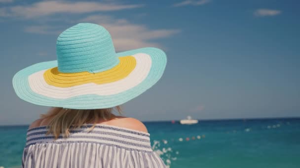 Una mujer con sombrero mira el mar azul. Concepto de vacaciones de sueño — Vídeos de Stock