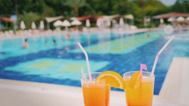 En lyxig semester för två älskande, två glas med en orange cocktail på bakgrunden av en enorm pool med turister — Stockvideo