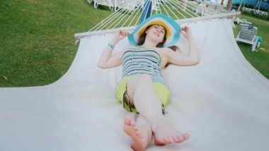 Serin parlak şapkalı bir genç kız bir tatil beldesi beyaz bir hamakta kalanını keyif alıyor
