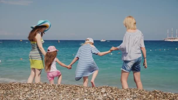 Meninas jovens com cerca de seus filhos pequenos se divertir na costa, saltar sobre as ondas, desfrutar do resto — Vídeo de Stock