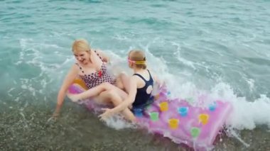 Bir anne ve bir çocuk ile bir şişme yatak büyük dalgalar deniz taşımak, eğlenceli bir dalgalar binmek