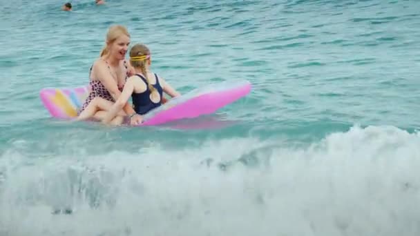 그녀의 젊은 어머니와 어린 딸은 적극적으로 휴식 해변 휴양지에 재미는 매트리스에 파도 위에 점프 — 비디오