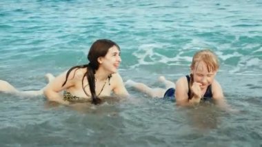 Bir kızla genç bir etkin anne eğlenceli plaj, dalgalar deniz üzerinde oynuyor gülüyor, somersaulting