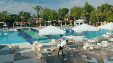 Kemer, Türkiye, Haziran 2018: Otel personeli toprakları beş yıldızlı otelin kaldırır. Tablolar ve şemsiyeler havuzun vardır - her şey Türkiye'de rahat rahat