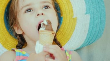 Bir şapka, sevimli küçük bir kız portresi. Çikolatalı dondurma yiyor. Yaz tatili çocuk kavramı ile