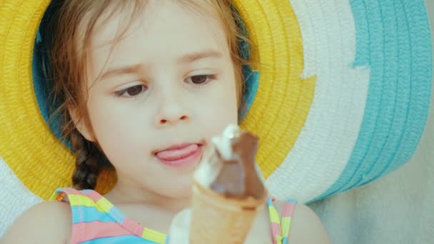 Портрет милой маленькой девочки в шляпе. Он ест шоколадное мороженое. Летние каникулы с детской концепцией — стоковое видео