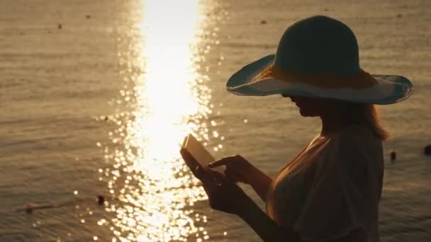 Een jonge vrouw maakt gebruik van een tablet tegen de achtergrond van de rijzende zon op een zee-pier. — Stockvideo